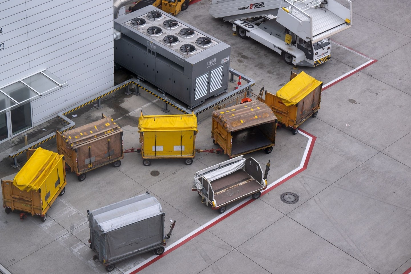 Gepäckwagen stehen am Flughafen München auf dem Rollfeld: Viele Fluggäste warten eine Woche nach ihrem Zwischenstopp in München noch immer auf ihr Gepäck.
